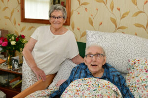 An elderly gentleman lying in bed with an elderly lady standing next to him