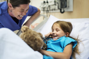 young girl in a hospital bed, laughing with a healthcare professional