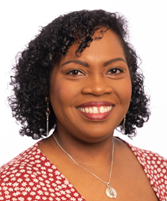 A person with curly hair wearing a red patterned top and a necklace with a pendant, posed against a plain white background.