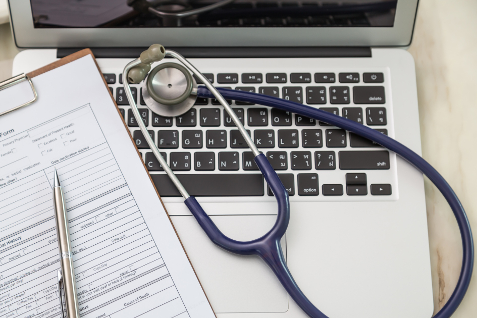 A laptop keyboard has a stethoscope across it, with a form on a clip board beside it.