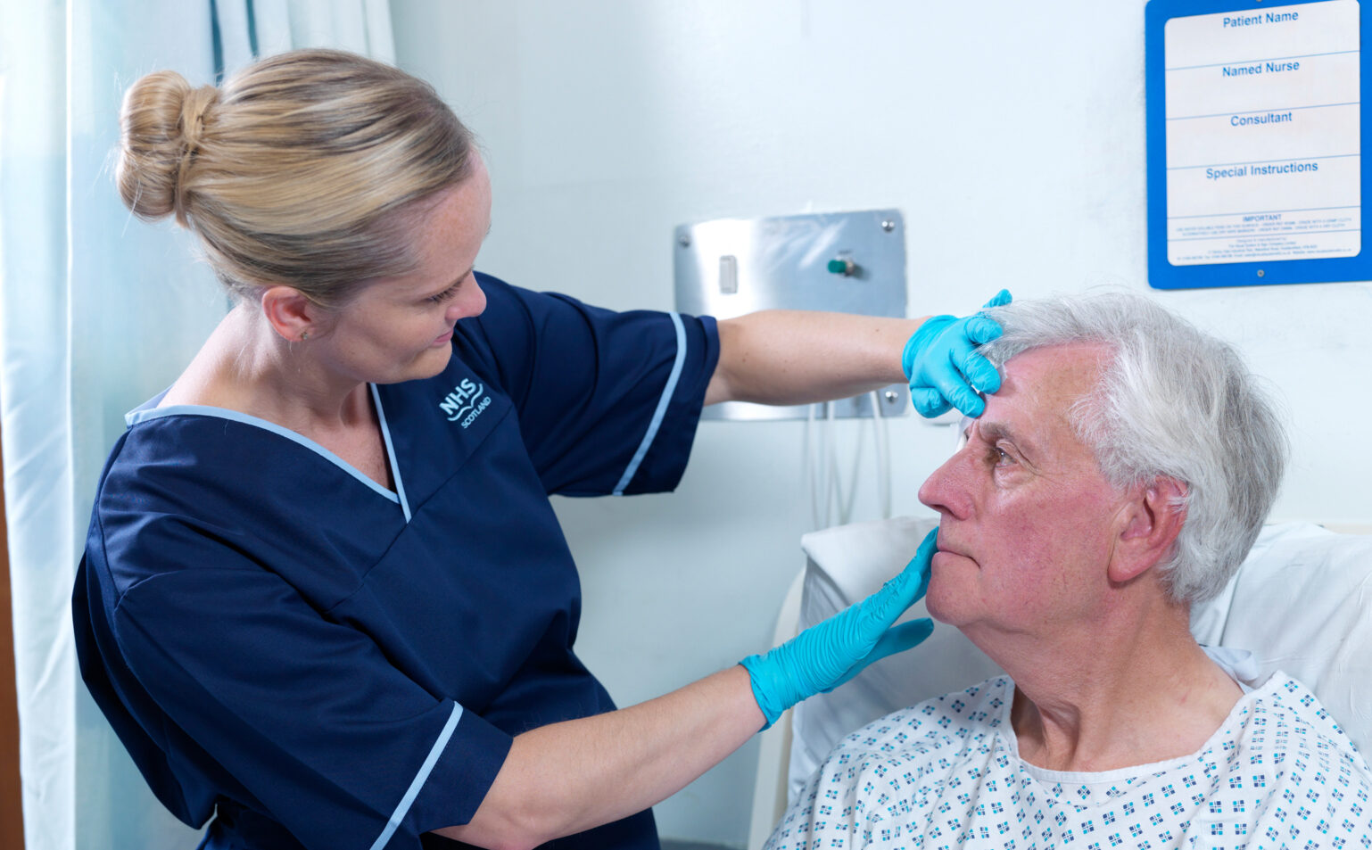 A nurse in blue NHS Scotland scrubs is examining an older patient's face. Text reads: "Updated change packages for adults in hospital."