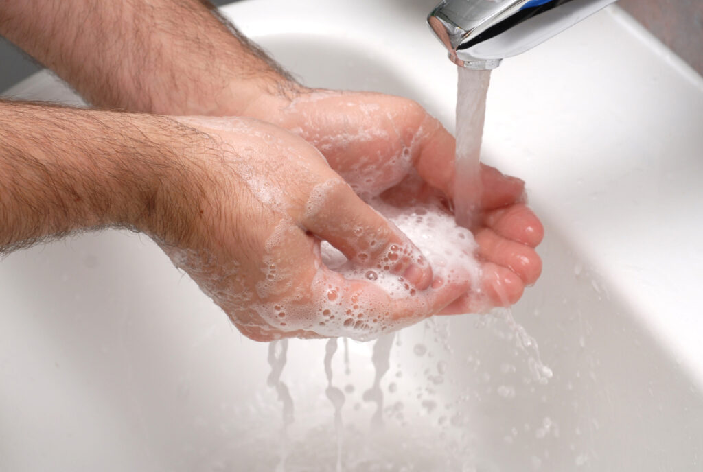 Two hands full of soap and water under a running tap